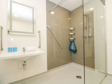 A bathroom with a wall-mounted sink mirror shower area with grab bars and shelving at Rowan in Truro