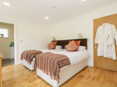 A bedroom with two single beds with brown blankets and orange pillows and white robes hanging on a wooden door at Rowan in Truro