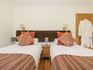 A bedroom with two single beds a wooden nightstand a door with a white robe hanging Rowan Truro