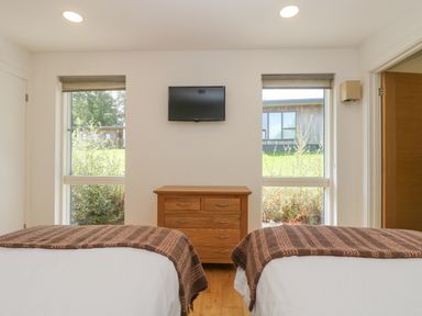 A bedroom with two beds a wooden chest of drawers and a wall-mounted television at Rowan in Truro