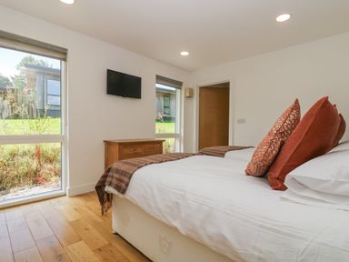 A bedroom with a bed with pillows a wooden chest of drawers and a wall-mounted TV at Rowan in Truro
