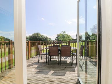 A wooden deck with a glass table and six chairs overlooking a grassy area and trees at Rowan in Truro
