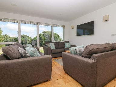 A living room with three sofas facing a wall mounted TV and large windows showing trees at Willow in Truro