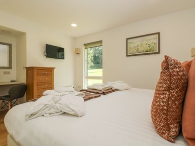 A bedroom with a bed with pillows and robes a wooden chest of drawers a wall mounted tv and a desk with a chair at Willow in Truro