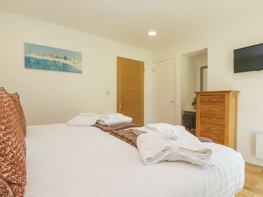 A bedroom with a bed with folded robes pillows a wooden chest of drawers a wall-mounted TV and a door at Willow in Truro
