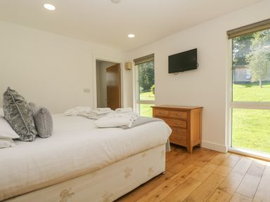A bedroom with a bed pillows towels a wooden dresser a wall mounted tv and windows showing a grassy area at Willow in Truro