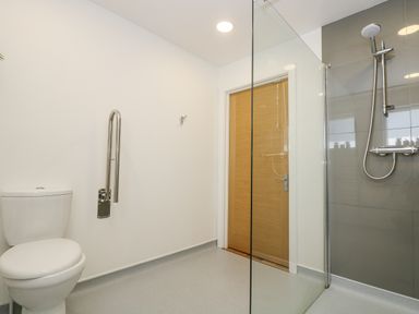 A bathroom with a toilet and a walk-in shower separated by a glass panel and a wooden door at Willow in Truro