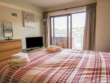 A bedroom with a bed covered with patterned bedding towels on top a TV on a stand a wooden dresser a floor lamp curtains and a sliding glass door overlooking water at Boavista Carnforth