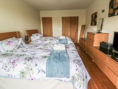 A bedroom with two single beds floral bedding wooden furniture and two closed wooden doors at Boavista Carnforth