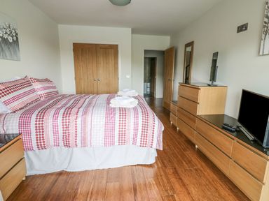 A bedroom with a bed with patterned bedding a wooden dresser with two televisions and a wooden floor at Boavista in Carnforth