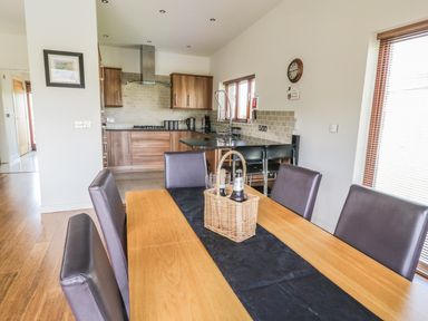 A dining area with a wooden table and black chairs next to a kitchen with wooden cabinets and tile backsplash at Boavista in Carnforth