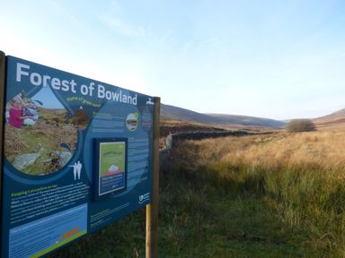 A wooden signboard about Forest of Bowland in a grassy open landscape with hills in the distance at Boavista in Carnforth