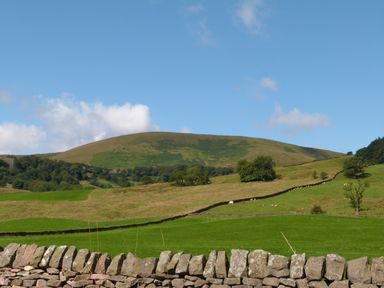 A hillside with green fields stone walls and trees under a blue sky at Boavista in Carnforth