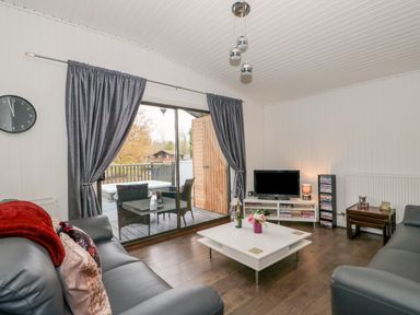 A living room with leather sofas a white coffee table a tv on a stand and glass sliding doors to a balcony at Sunset Lodge in Tattershall