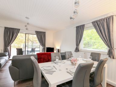 A dining area with a table set for six and a living room with sofas and curtains at Sunset Lodge in Tattershall