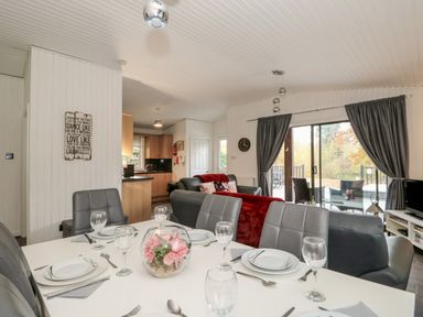 A dining table set with plates and glasses in an open living room with sofas and sliding glass doors at Sunset Lodge in Tattershall