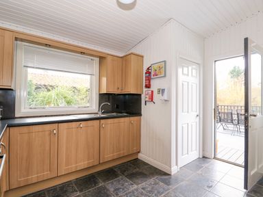 A kitchen with wooden cabinets and a sink under a window with a door leading outside at Sunset Lodge in Tattershall