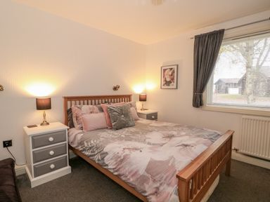 A bedroom with a wooden bed and floral bedding beside two nightstands with lamps and a window with curtains at Sunset Lodge in Tattershall
