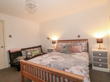 A bedroom with a wooden double bed floral bedding two bedside tables with lamps and a black futon at Sunset Lodge in Tattershall