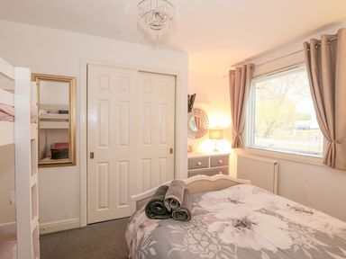 A bedroom with a bed covered with floral bedding and rolled towels on top a window with curtains a dresser with a lamp and mirror and a closet with sliding doors at Sunset Lodge in Tattershall