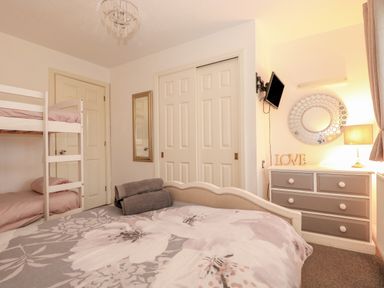 A bedroom with a double bed and bunk beds a dresser with a lamp and circular mirror and a wall mounted tv at Sunset Lodge in Tattershall
