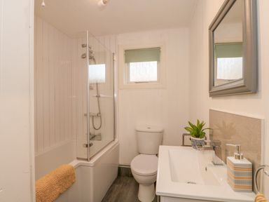 A bathroom with a bathtub shower combination toilet sink mirror and small window at Sunset Lodge in Tattershall