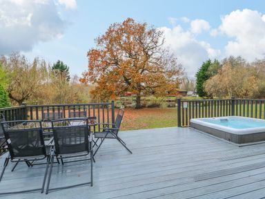 An outdoor deck with black chairs and a table next to a hot tub overlooking a lawn with a large tree at Sunset Lodge in Tattershall