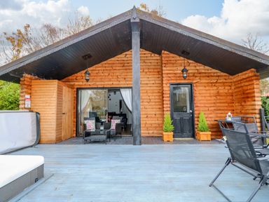 A wooden cabin exterior with a deck having outdoor chairs and a table at Sunset Lodge in Tattershall