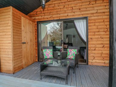 A patio with two chairs with floral cushions and a glass coffee table outside a wooden cabin at Sunset Lodge in Tattershall