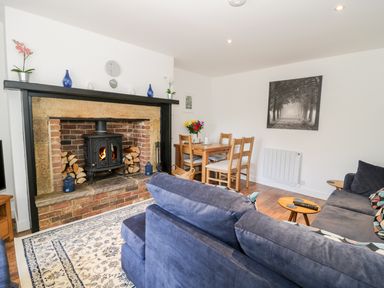 A living room with a wood burning stove fireplace a blue sofa a wooden dining table and chairs at Skovhaven in Catton
