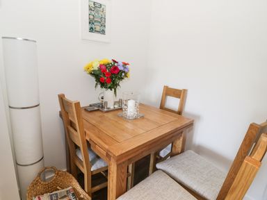 A small wooden dining table with four chairs a vase of flowers on the table and a tall floor lamp against the wall at Skovhaven in Catton