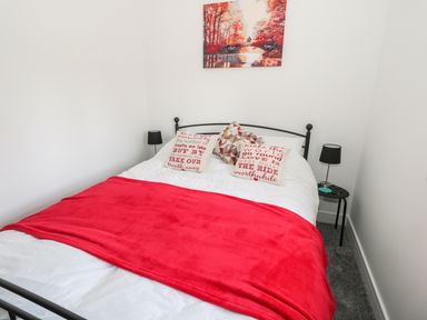 A bedroom with a bed covered with white and red bedding two bedside tables with black lamps and a wall painting of a red forest at Skovhaven in Catton