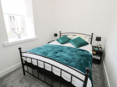 A bedroom with a black metal bed frame a teal blanket and pillows a window with a candle holder and two bedside tables with lamps at Skovhaven in Catton