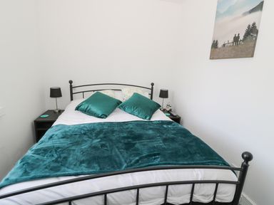 A bedroom with a black metal bed frame teal pillows and blanket two bedside tables with lamps and a wall picture at Skovhaven in Catton