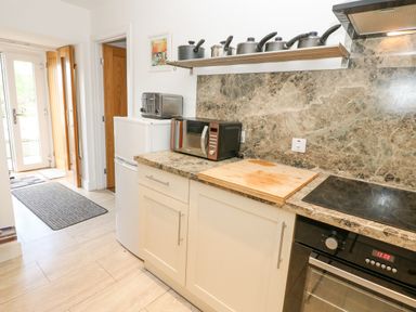 A kitchen countertop with a microwave chopping board and stove a toaster and pots on a shelf at Skovhaven in Catton