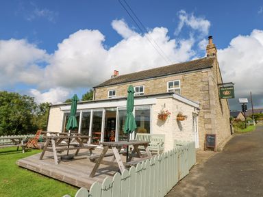 A stone building with outdoor picnic tables and green umbrellas on a wooden deck at Skovhaven in Catton