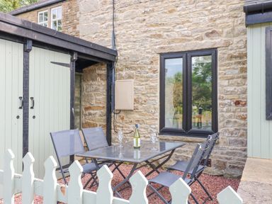 An outdoor seating area with a metal table and four chairs next to a stone wall and window at Skovhaven in Catton