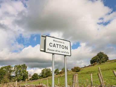 A road sign that says welcome to catton with a grassy field and trees in the background at Skovhaven in Catton