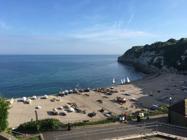 A pebble beach with boats and a calm sea next to cliffs at Pottery Barn in Branscombe
