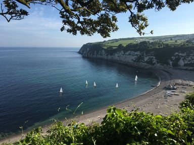 A beach with sailboats on the water cliffs and houses in the background at Pottery Barn in Branscombe