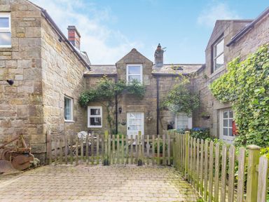 A stone courtyard with wooden fences and green plants outside a stone house at Briar Cottage in Edlingham