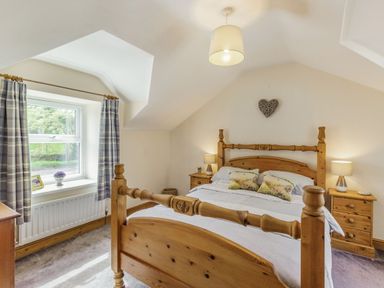 A bedroom with a wooden bed and bedside tables with lamps at Briar Cottage in Edlingham
