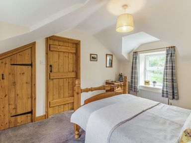 A bedroom with a wooden bed, two wooden doors, a window with checkered curtains and a small dresser at Briar Cottage in Edlingham