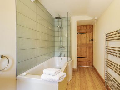 A bathroom with a bathtub shower towels a wooden door and a metal towel rack at Briar Cottage in Edlingham