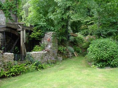 A garden with dense green foliage and an old stone water wheel structure at Water Barn in Manaton near Lustleigh