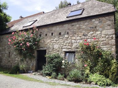 Stone barn exterior with two skylights a black door and window surrounded by rose bushes at Water Barn in Manaton near Lustleigh