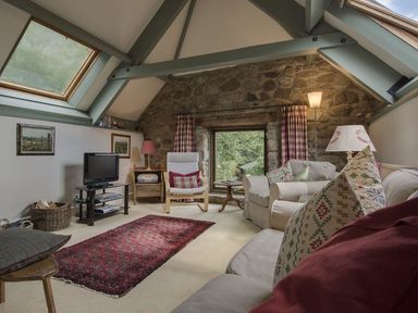 A living room with a stone wall small window sofas armchair TV and skylights at Water Barn in Manaton near Lustleigh