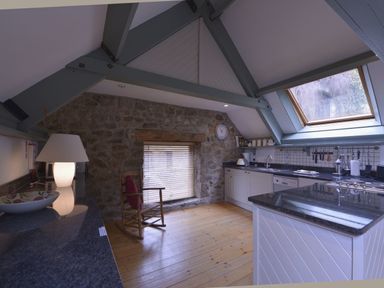 A kitchen with stone walls wooden floor a rocking chair and a skylight window at Water Barn in Manaton near Lustleigh