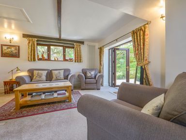 A living room with a sofa armchair wooden coffee table and floral curtains at Buster Barn in Sampford Spiney near Tavistock