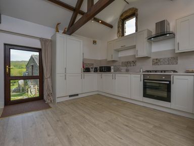 A kitchen with white cabinets a built-in oven a window above the sink and a glass door showing an outside view at Buster Barn in Sampford Spiney near Tavistock
